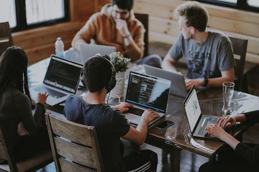 A group of professionals seated at a table, each using laptops, collaborating on strategies to identify key decision-makers.